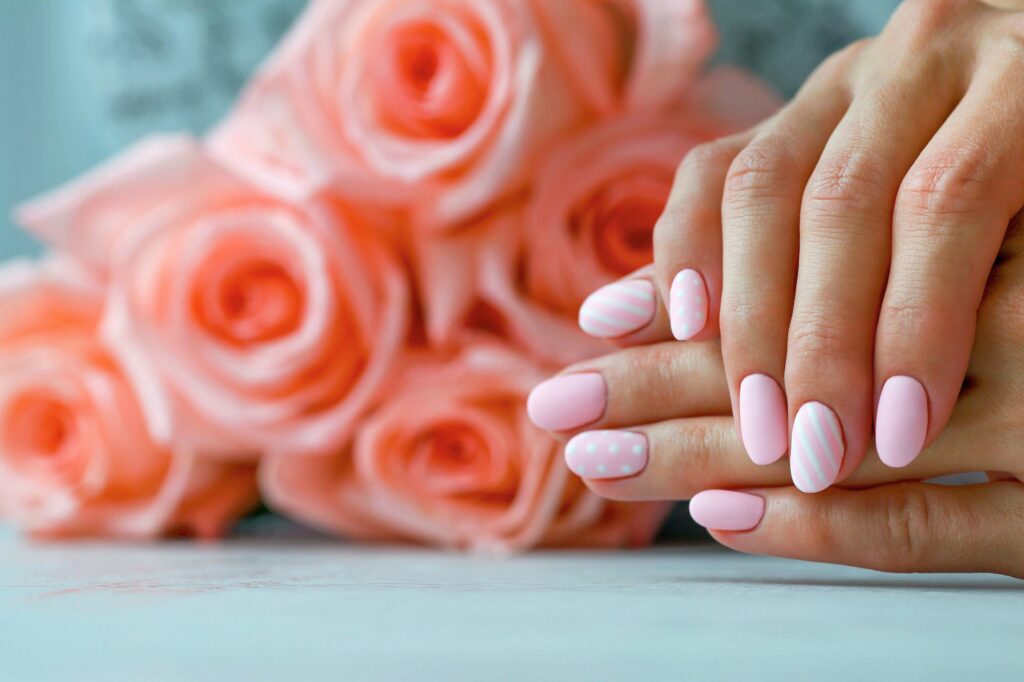 Beautiful pink matte manicure against the background of roses. Gel silk, oval-shaped nails.